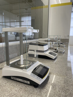Mulher de jaleco e óculos de segurança opera máquina industrial em laboratório do Instituto Mauá de Tecnologia.