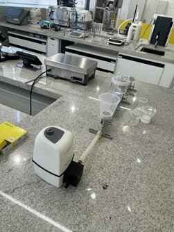 Dois homens em um laboratório de engenharia, um aponta para um painel de controle complexo com fios.