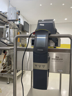 Dois homens em um laboratório de engenharia, um aponta para um painel de controle complexo com fios.