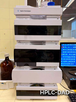 Dois homens em um laboratório de engenharia, um aponta para um painel de controle complexo com fios.