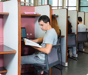 Estudante concentrado lendo livro em cabine individual de estudo no Instituto Mauá de Tecnologia.