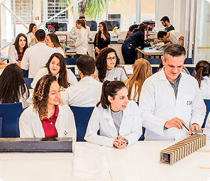 Estudantes e professor em laboratório do Instituto Mauá de Tecnologia, com jalecos brancos, em atividade prática.