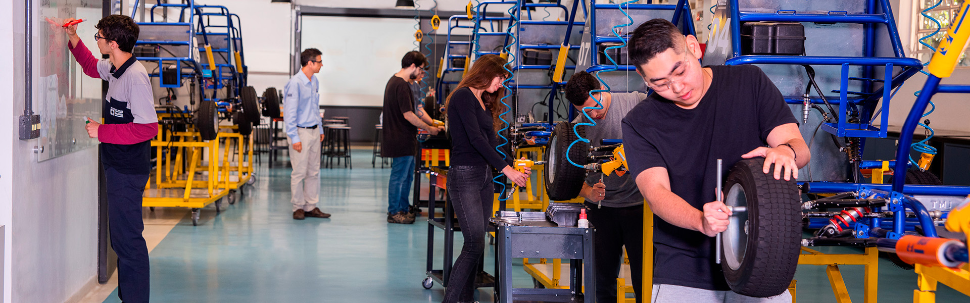 Estudantes do Instituto Mauá de Tecnologia trabalham em um laboratório com karts e ferramentas.
