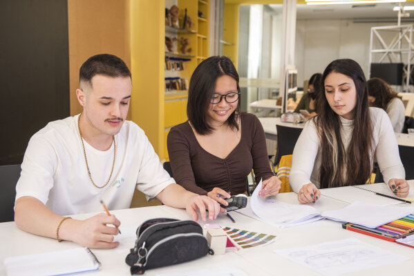 Estudantes do Instituto Mauá de Tecnologia trabalham em projetos, com papéis, lápis e amostras de cores sobre a mesa.