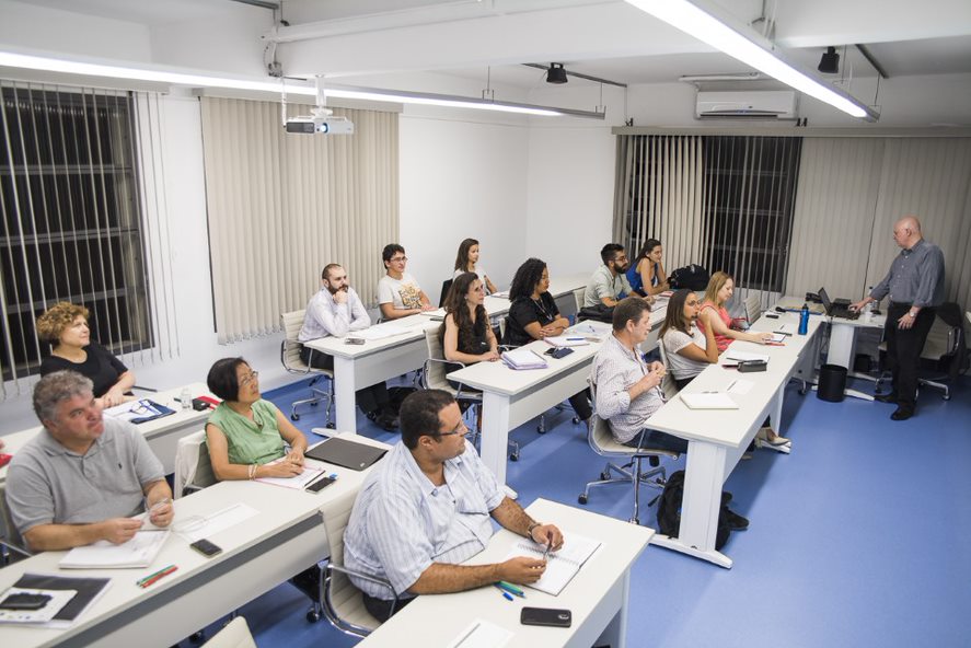 Sala de aula com alunos sentados em mesas e um professor em pé, no Instituto Mauá de Tecnologia.