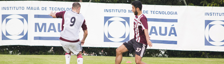 Jogadores de futebol em campo, com banner do Instituto Mauá de Tecnologia ao fundo.