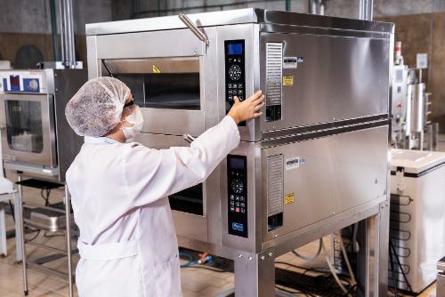 Mulher de jaleco e óculos de segurança opera máquina industrial em laboratório do Instituto Mauá de Tecnologia.