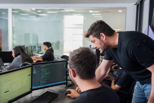 Um homem ensina outro a programar em um laboratório de informática com vários computadores.