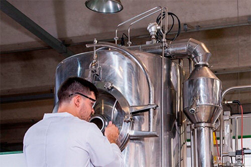 Dois homens em um laboratório de engenharia, um aponta para um painel de controle complexo com fios.