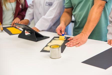 Pessoas em laboratório aplicam tinta amarela em papel preto com rolo.