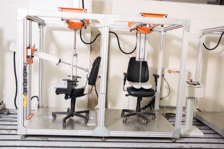 Cadeiras de escritório em estrutura metálica para testes de resistência, com equipamentos de medição e controle.
