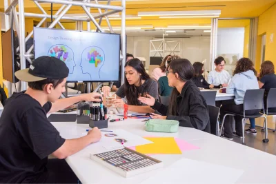 Estudantes em sala de aula do Instituto Mauá de Tecnologia trabalham em projetos, com tela exibindo "Design Thinking - Empatia".