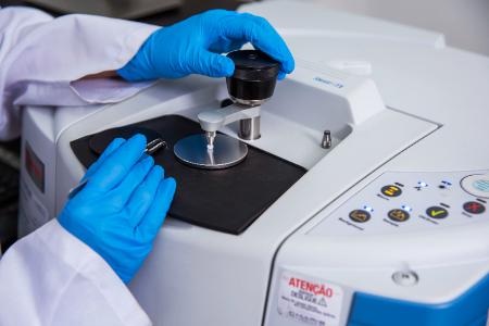 Mãos com luvas azuis operando equipamento de laboratório com superfície espelhada.