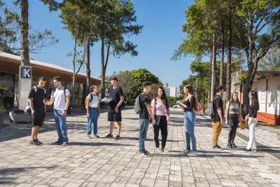 Estudantes do Instituto Mauá de Tecnologia conversam em um pátio ensolarado com prédios e árvores ao fundo.