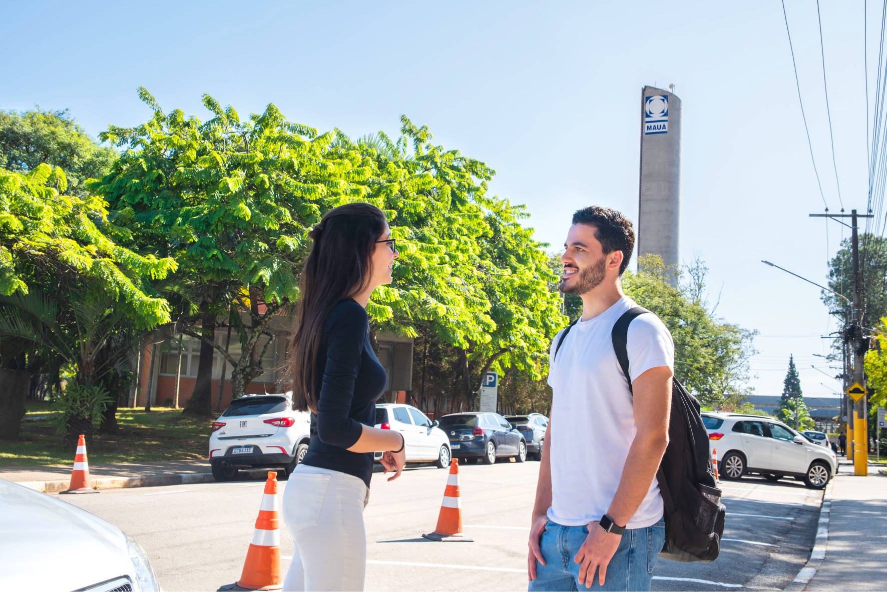 Duas pessoas conversando em frente à torre do Instituto Mauá de Tecnologia em um dia ensolarado.
