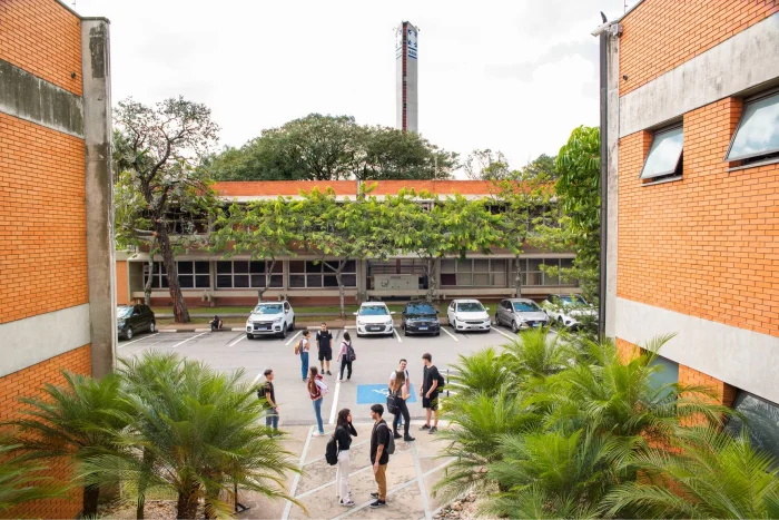 Estudantes em um estacionamento no Instituto Mauá de Tecnologia, com carros e um prédio ao fundo.