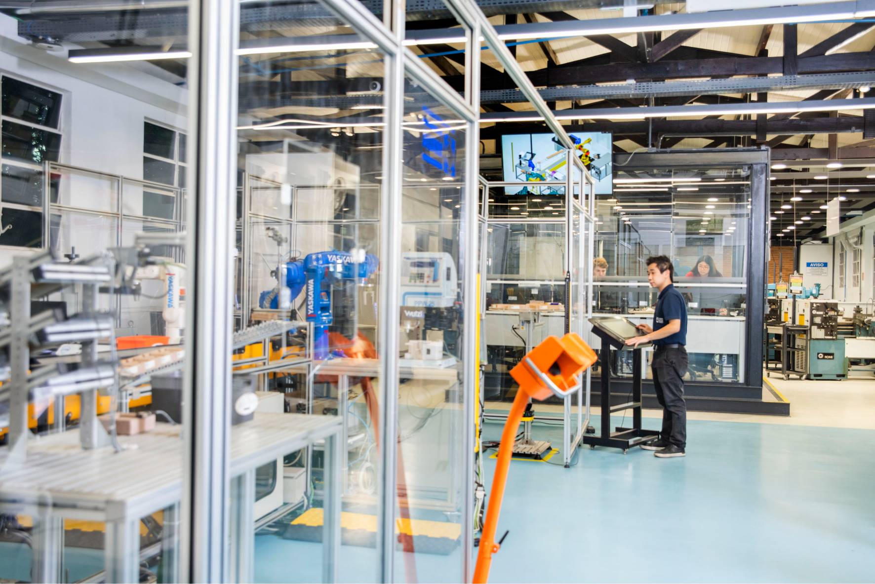 Robô industrial Yaskawa em laboratório de automação, com estudante operando console.