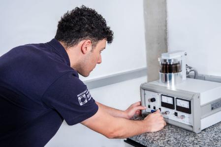 Homem ajustando equipamento de laboratório com medidores e recipiente cilíndrico.